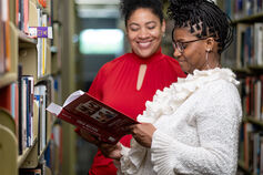 Two adults reading a book on child welfare in a library.